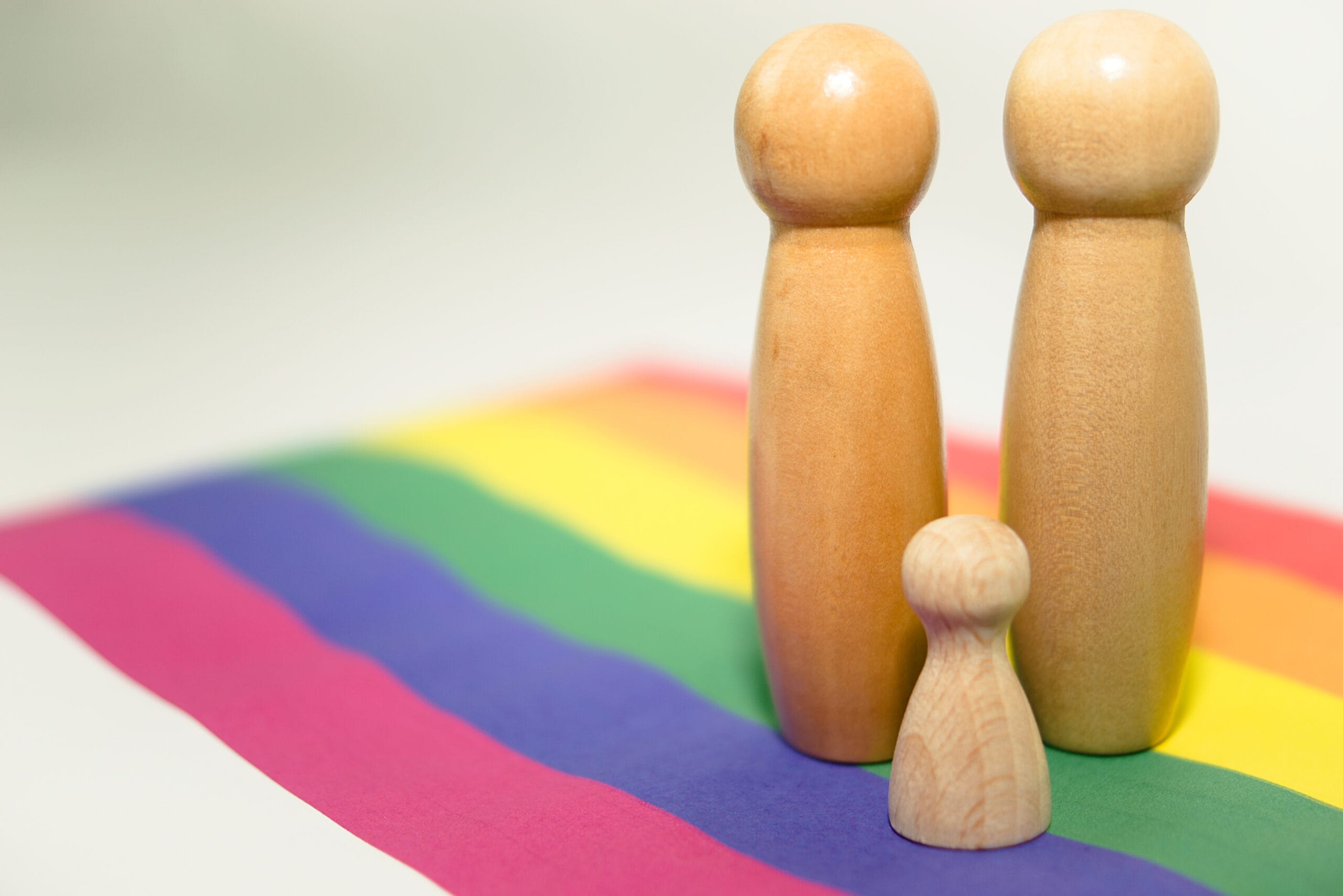 three wooden figures on a rainbow background, same-sex figures, systemic board, family therapy